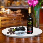 A 200ml bottle of Black Cherry Balsamic Vinegar on white plate with black cherries and sample balsamic vinegar