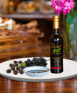 A 200ml bottle of Black Cherry Balsamic Vinegar on white plate with black cherries and sample balsamic vinegar