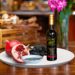 A 200ml bottle of Pomegranate Balsamic on white plate with pomegranate and sample balsamic vinegar
