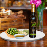 A 200 ml bottle of Biancolilla Olive Oil on white plate with olives from Italy, artichoke and sample olive oil