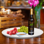 A 200ml bottle of Cascadian Wild Raspberry White Balsamic Vinegar on white plate with wild raspberries and sample balsamic vinegar