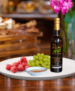 A 200ml bottle of Cascadian Wild Raspberry White Balsamic Vinegar on white plate with wild raspberries and sample balsamic vinegar