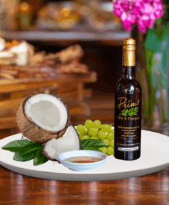 A 200ml bottle of Coconut Balsamic Vinegar on white plate with coconut and sample balsamic vinegar