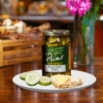 A jar of Bread and butter pickles on white plate with butter on bread and sliced cucumber