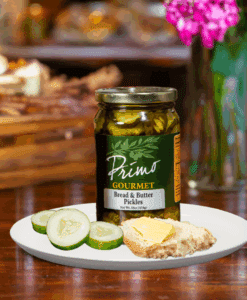 A jar of Bread and butter pickles on white plate with butter on bread and sliced cucumber
