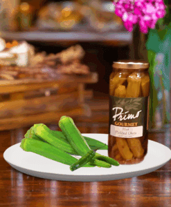 A jar of Hot Pickled Okra on white plate with okra and green chili pepper