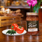 A jar of Hot Summer Tomato Salsa with tomatoes and green chili peppers on white plate