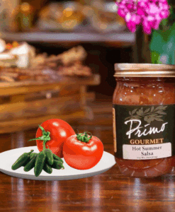 A jar of Hot Summer Tomato Salsa with tomatoes and green chili peppers on white plate