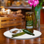 A jar of Zesty Pickled Asparagus on white plate with asparagus and green chili pepper