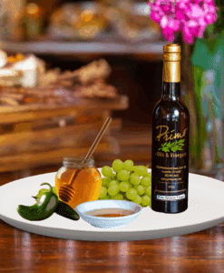 A 200ml bottle of Serrano Honey Vinegar on white plate with honey, green chili pepper and sample balsamic vinegar