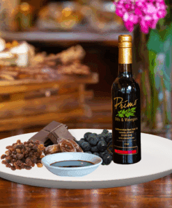 A 200ml bottle of Denissimo Balsamic Vinegar on white plate with fruits, raisins, figs, dark chocolate and sample balsamic vinegar