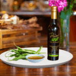 A 200 ml bottle of Baklouti Green Chili Oil on white plate with Baklouti chilies and sample chili oil