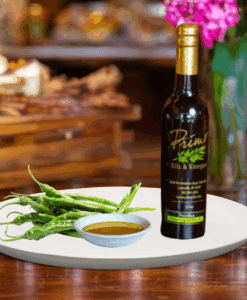 A 200 ml bottle of Baklouti Green Chili Oil on white plate with Baklouti chilies and sample chili oil