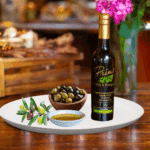 A 200ml bottle of Coratina EVOO on white plate with bowl of olives grown in Peru and sample olive oil