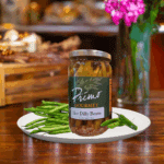 A jar of Hot Dilly Beans on white plate with green beans and green chili pepper.