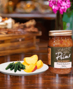 A jar of Peach Habanero Salsa and chili green peppers and slice peaches on white plate