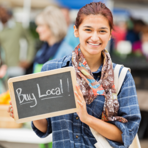 woman at a farmers market holds a sign that reads buy local
