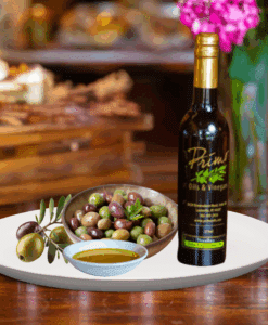 A 200ml bottle of Frantoio Extra Virgin Olive Oil on white plate with bowl of green and purple olive grown from Chile and sample olive oil