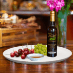 A 200ml bottle of Montmorency Cherry Rosé Balsamic Vinegar on white plate with cherries and sample balsamic vinegar